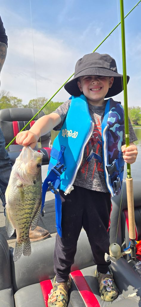 Young boy holding a bonus bass and fishing pole during a father and son guided crappie fishing trip on Rend Lake